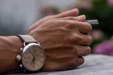 person wearing silver-colored chronograph watch leaning on gray surface HD wallpaper