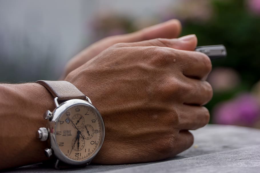 person wearing silver-colored chronograph watch leaning on gray surface HD wallpaper