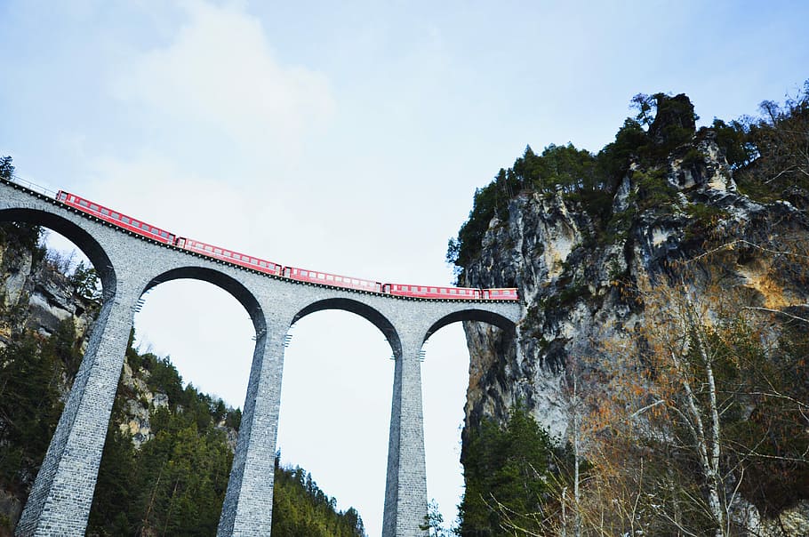 bridge with red train, low-angle photography of red train passing on gray concrete train rail connected to mountain tunnel during daytime HD wallpaper