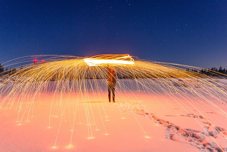 steel wool photography of person wearing black coat between tall trees during nighttime HD wallpaper