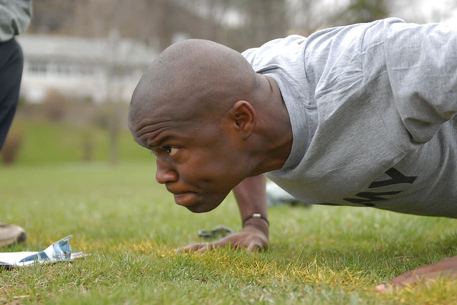 man wearing gray army shirt doing push up on the field, exercise