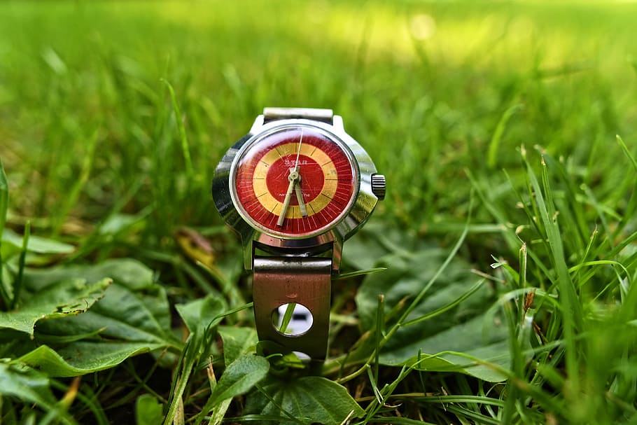 round silver-colored analog watch with brown band displaying at 5:32 on green grass field