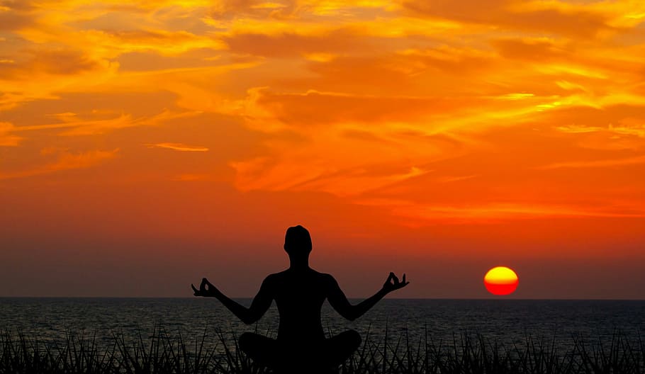  A person sits in a meditative pose on a beach at sunset.