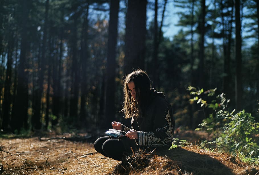 woman wearing black and gray top sitting during daytime, woman sitting on the rock holding a book