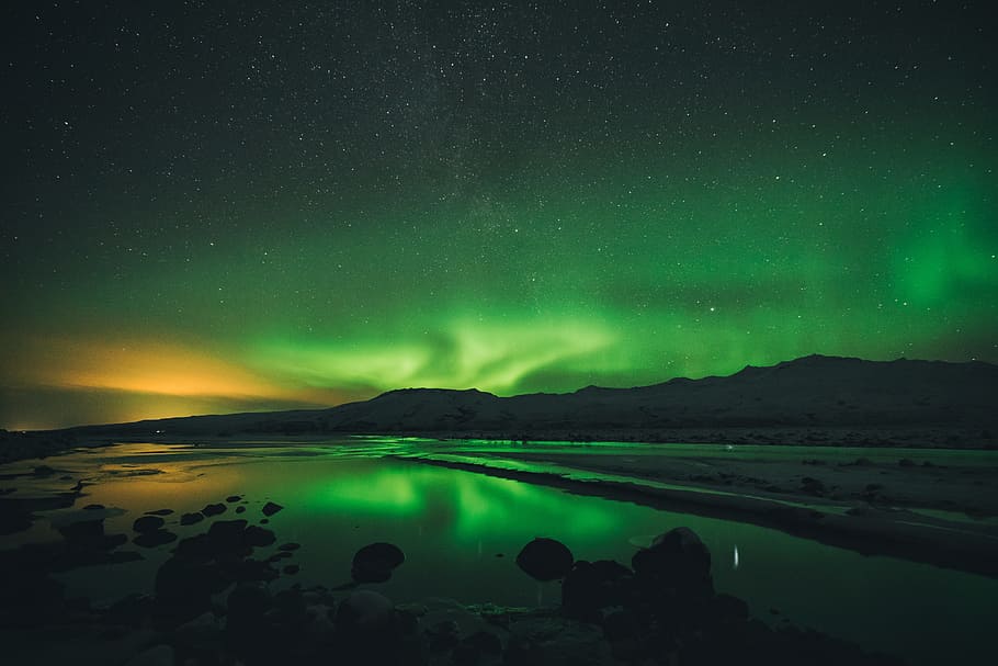calm of water near mountain under aurora borealis at night time, green northern lights