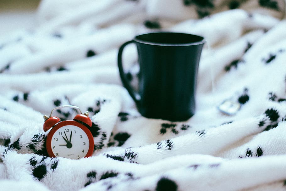 green ceramic mug beside red alarm clock on white and black textile closeup photo HD wallpaper