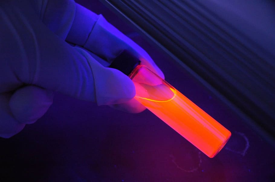 person with glove holding clear tube with orange liquid, glowing