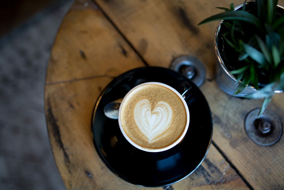 cup with heart capuccino on table, shallow focus photograph of teacup latte art beside plant