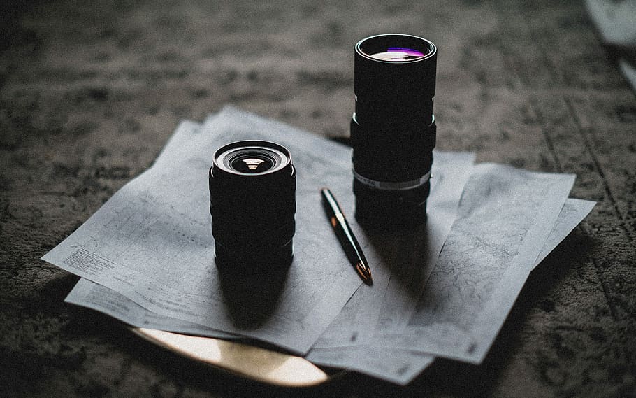 two camera lens on top of white printed papers and black and gold click pen, two black zoom lenses on gray printer paper next to fountain pen HD wallpaper