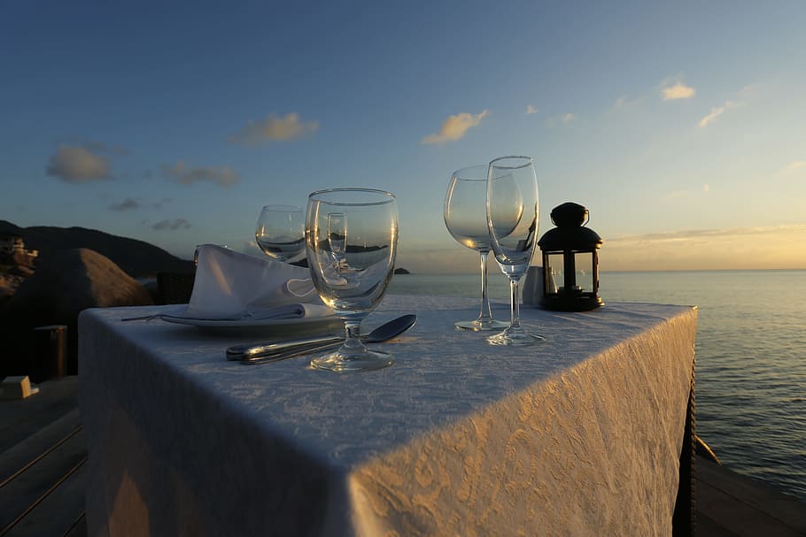 four empty wine glasses on white tablecloth near body of water at golden hour HD wallpaper