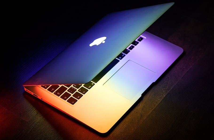 A MacBook lit up in rainbow colors on a wooden surface, flat lay photography of turned on silver MacBook HD wallpaper