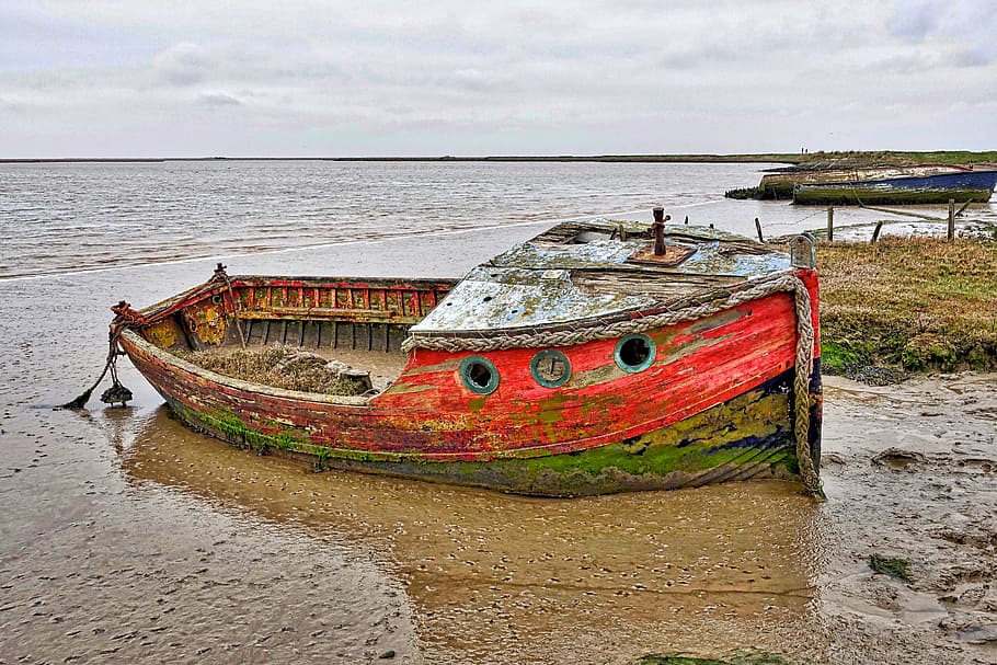 red wooden boat near body of water during daytime, beached, fishing