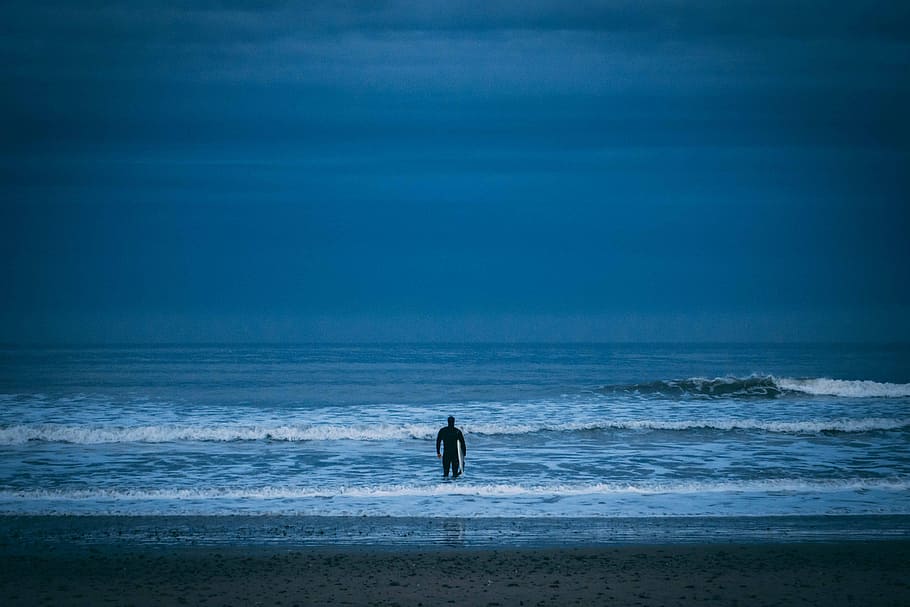 man standing on beach under cloudy sky, person swimming on ocean HD wallpaper