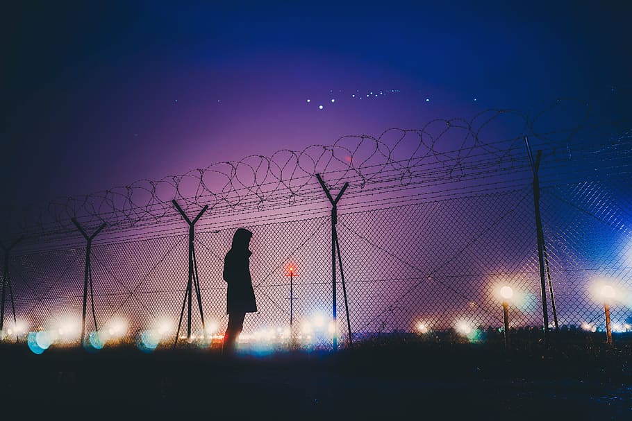 silhouette photograph of person standing beside link fence HD wallpaper