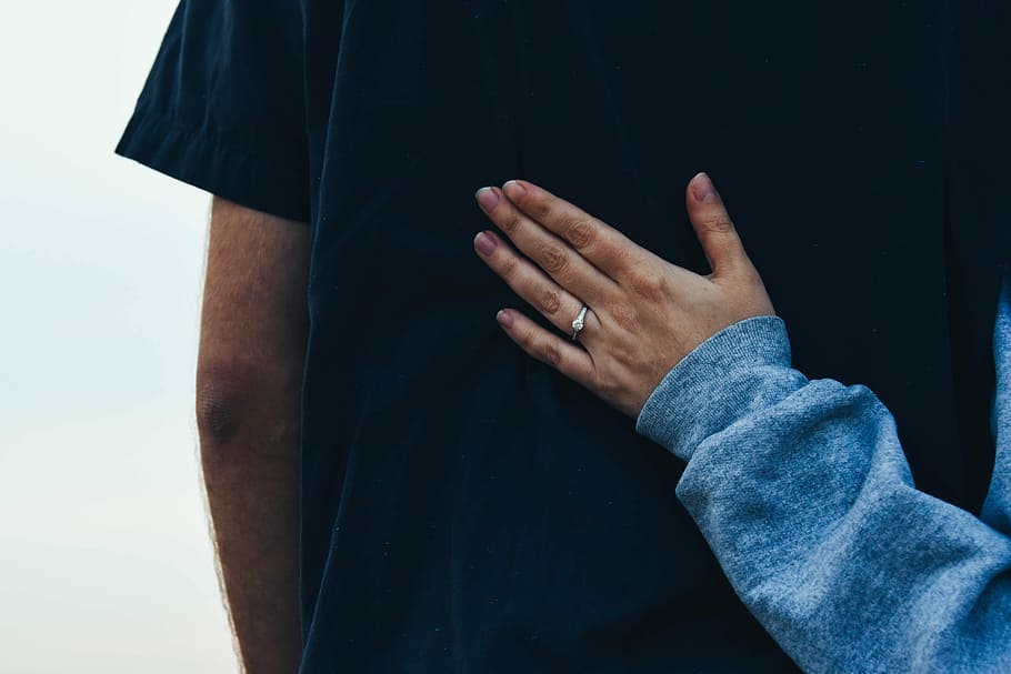 person wearing blue long-sleeved shirt resting its hand on man wearing black shirt, woman holding man back during daytime HD wallpaper