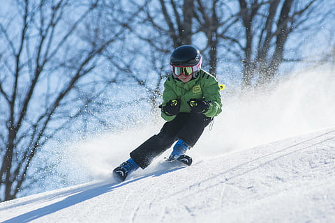 person wearing green ski jacket and snow goggles skiing over snow ground with distance at bare trees during daytime HD wallpaper