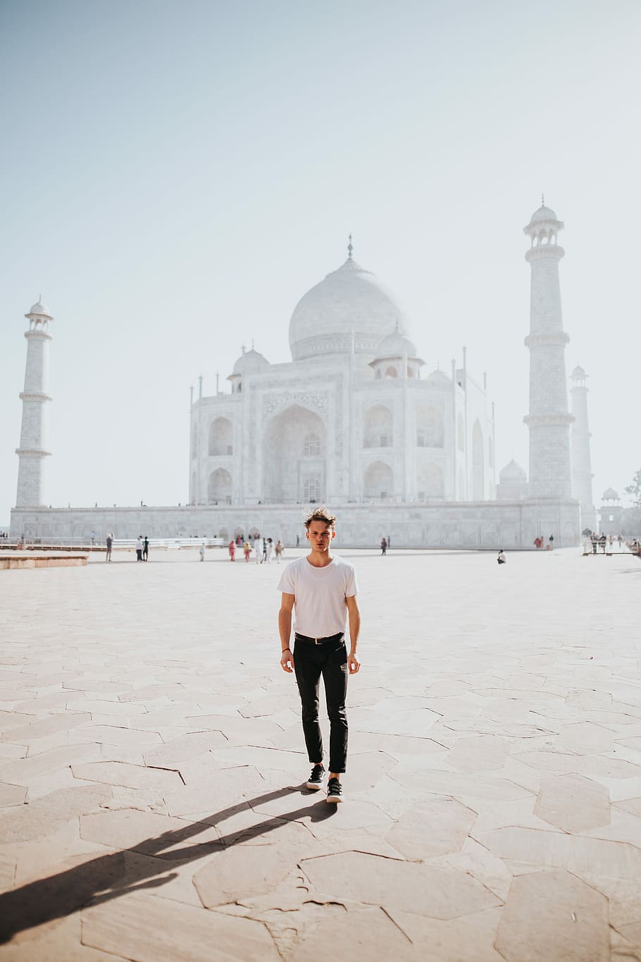 man standing near Taj Mahal, India, white concrete dome church behind man wearing white t-shirt and black pants standing on ground during daytime