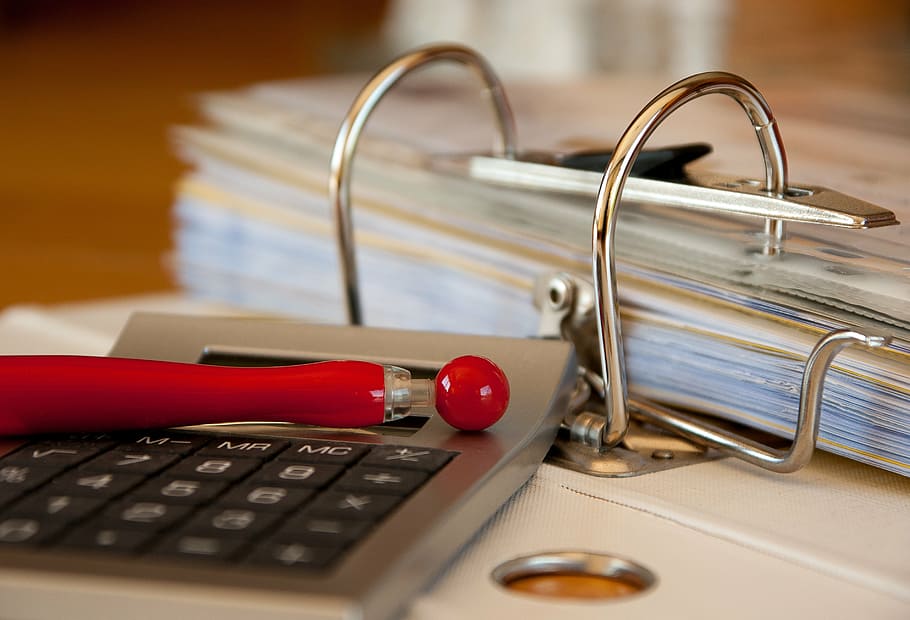 gray desk calculator beside pile of papers, workbook, bills, accounting