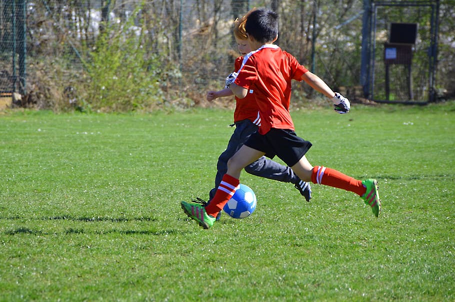 two boy playing soccer on green grass field during day time HD wallpaper