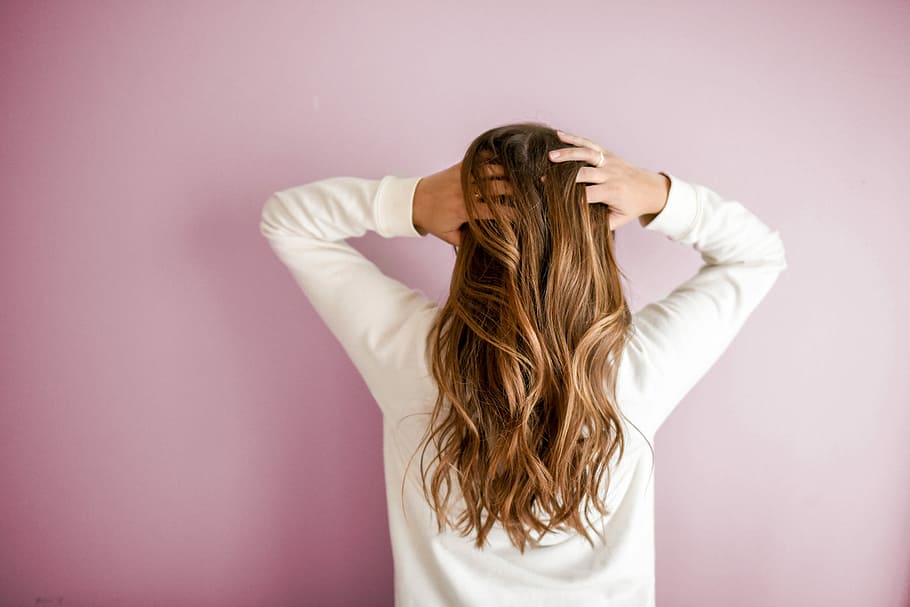 woman in white long-sleeved shirt standing in front of pink wall, woman holding her hair HD wallpaper