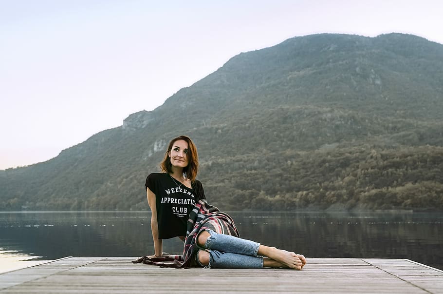 woman posing on dock located across the mountain, person sitting on wooden dock near body of water HD wallpaper