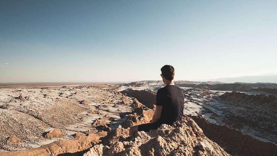 A lot more to explore, man sitting on rock formation outdoors HD wallpaper