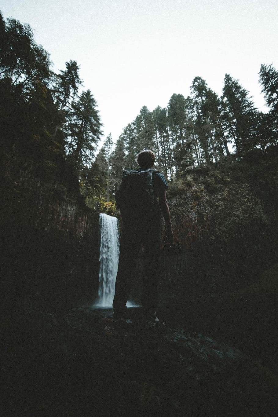 man standing in front of waterfalls at daytime, man standing on cliff facing waterfalls HD wallpaper