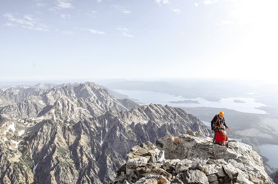 photo of man on top of mountain during daytime, two person standing on rocky cliff HD wallpaper