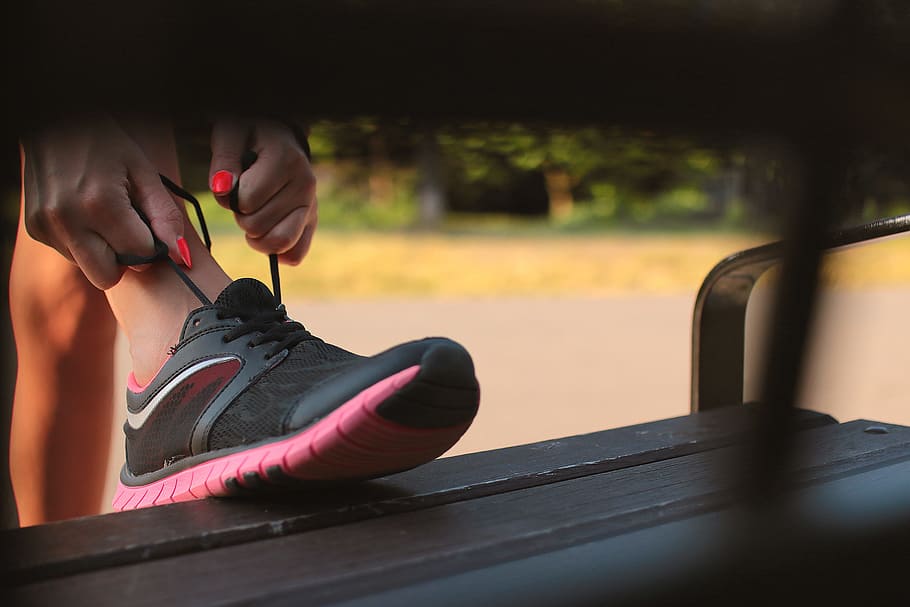 Woman in Black and Pink Sneaker Tying Lace of Her Shoe, female