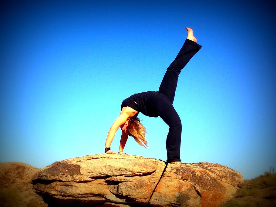 woman doing yoga post on rock formation, backbend, blue sky, fitness