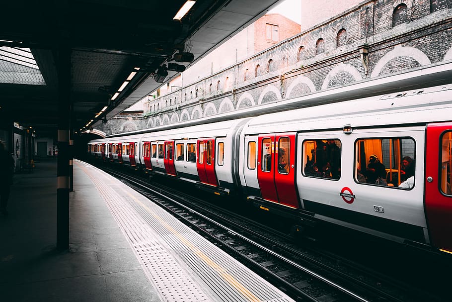 white and red train beside building at daytime, gray and red train with passengers inside HD wallpaper
