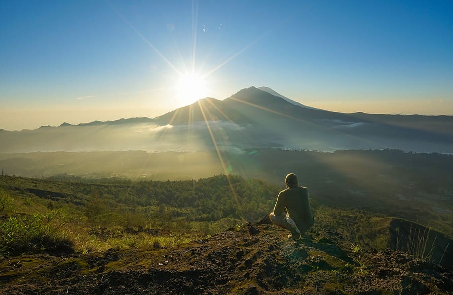 man squatting on mountain top during daytime, man sitting on mountain cliff looking at sunrise HD wallpaper