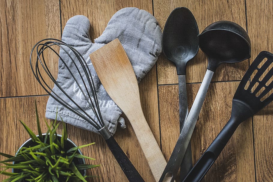 assorted kitchen utensils on brown wooden top, glove, plate, spoon