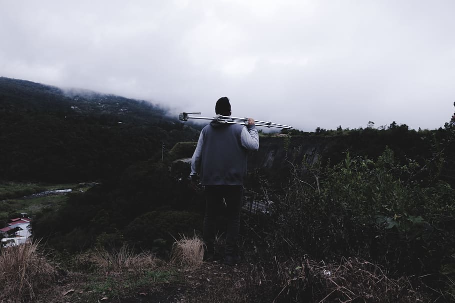 man holding gray metal stand surrounded grass, man holding tripod stand HD wallpaper