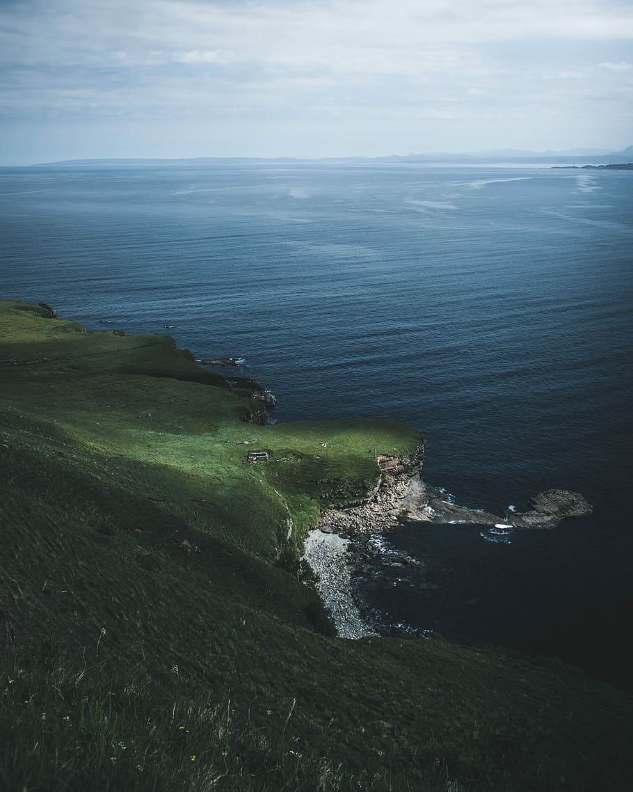 aerial photography of body of water near green land, green grass field mountain beside sea under cloudy sky HD wallpaper