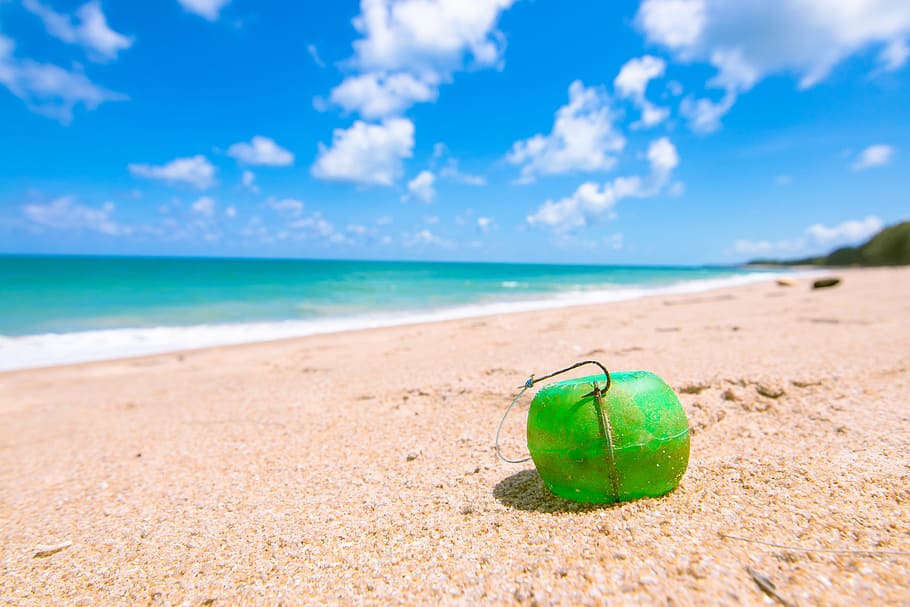 selective focus photography of green plastic container on seashore