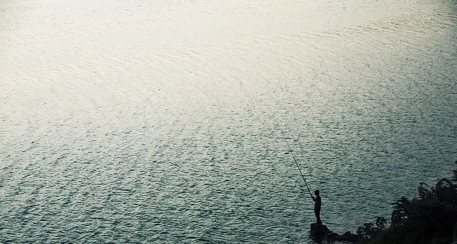 person stand on rock near body of water during daytime, silhouette of person holding fishing rod HD wallpaper