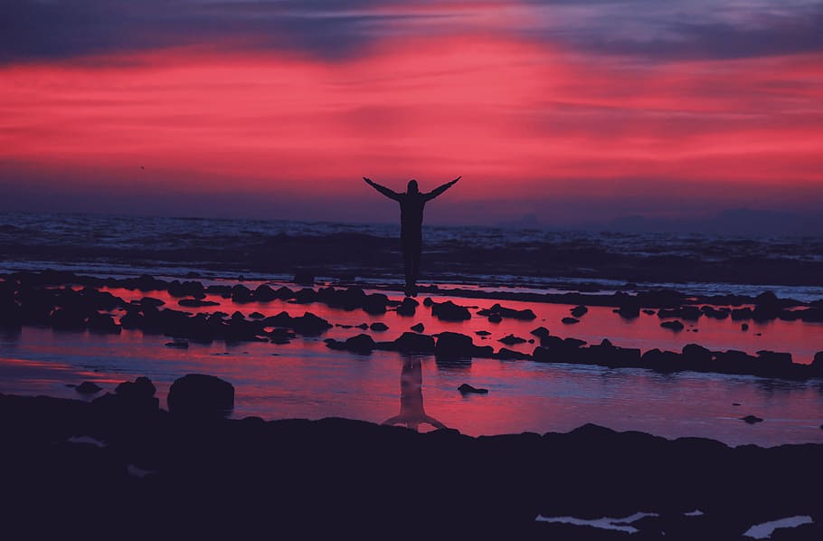 person standing on seashore while raising hands during sunset HD wallpaper