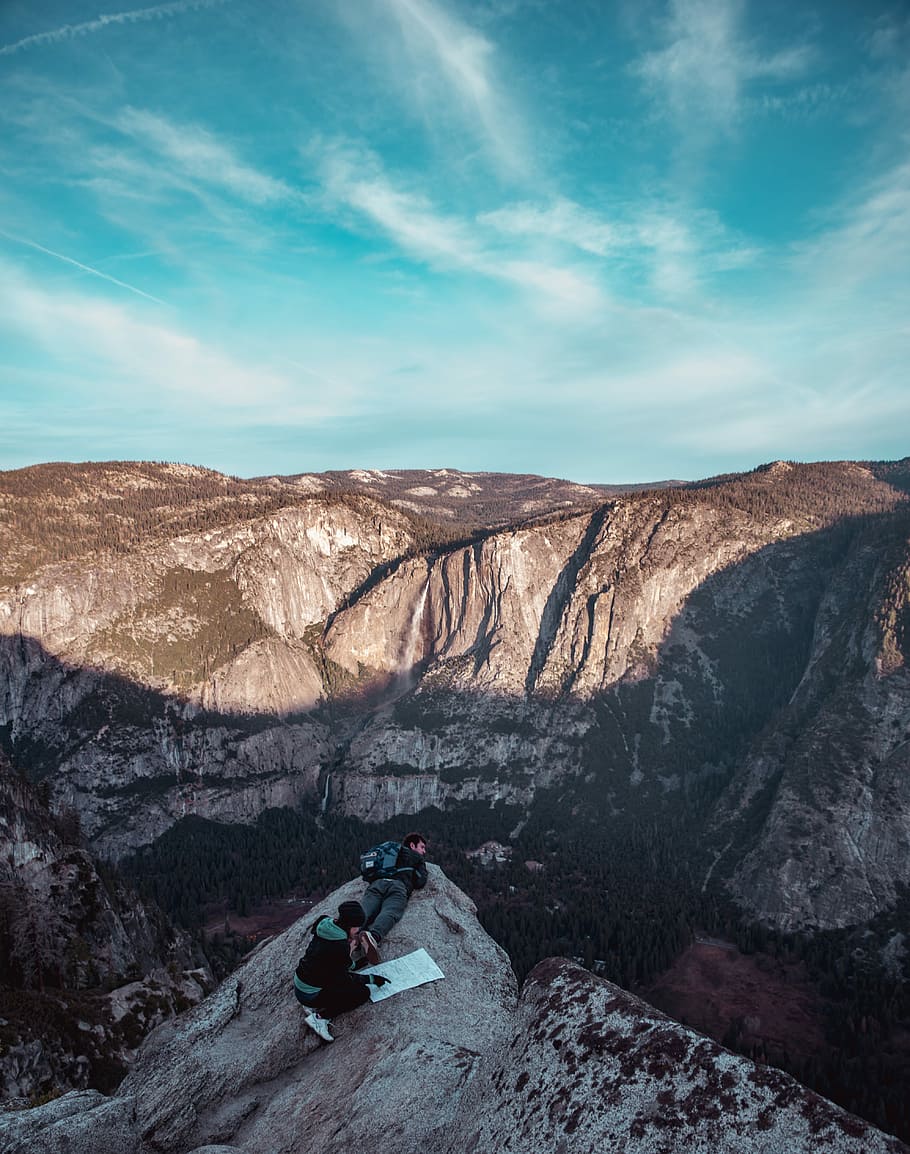 mountain rage view under blue sky during daytime, person kneeling beside man lying on edge of top of mountain HD wallpaper