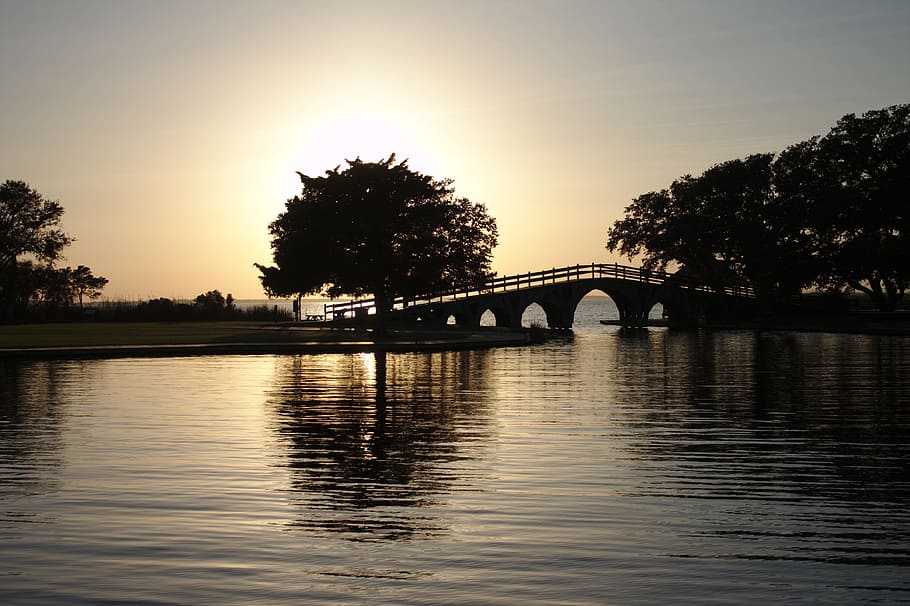 silhouette photo of bridge above rippling body of water during golden hour