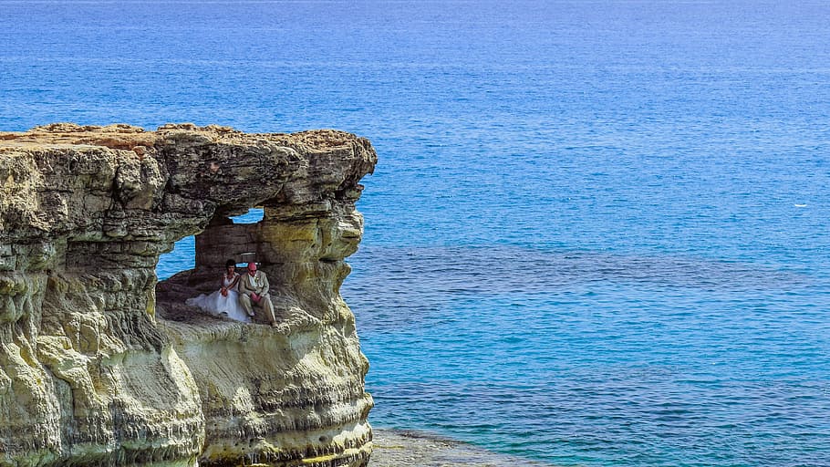 couple sitting on a cliff cave near ocean at daytime, rock HD wallpaper