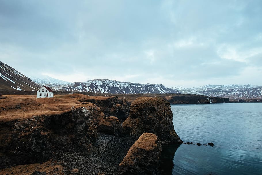 white and blue house on cliff near sea, gray stone cliff beside body of water HD wallpaper