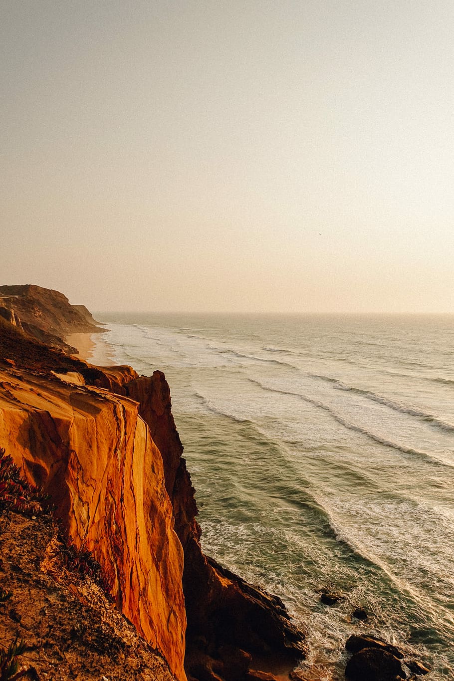 brown and black rock cliff beside ocean water during daytime, cliff near body of water HD wallpaper