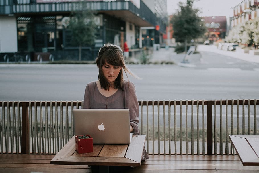 woman in gray shirt sitting on bench in front of MacBook, woman in grey 3/4 sleeve top facing MacBook on brown table HD wallpaper