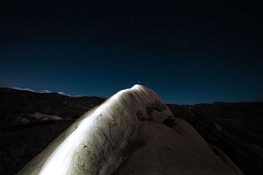 closeup photo of mountain during nighttime, person standing on white cliff during nighttime HD wallpaper