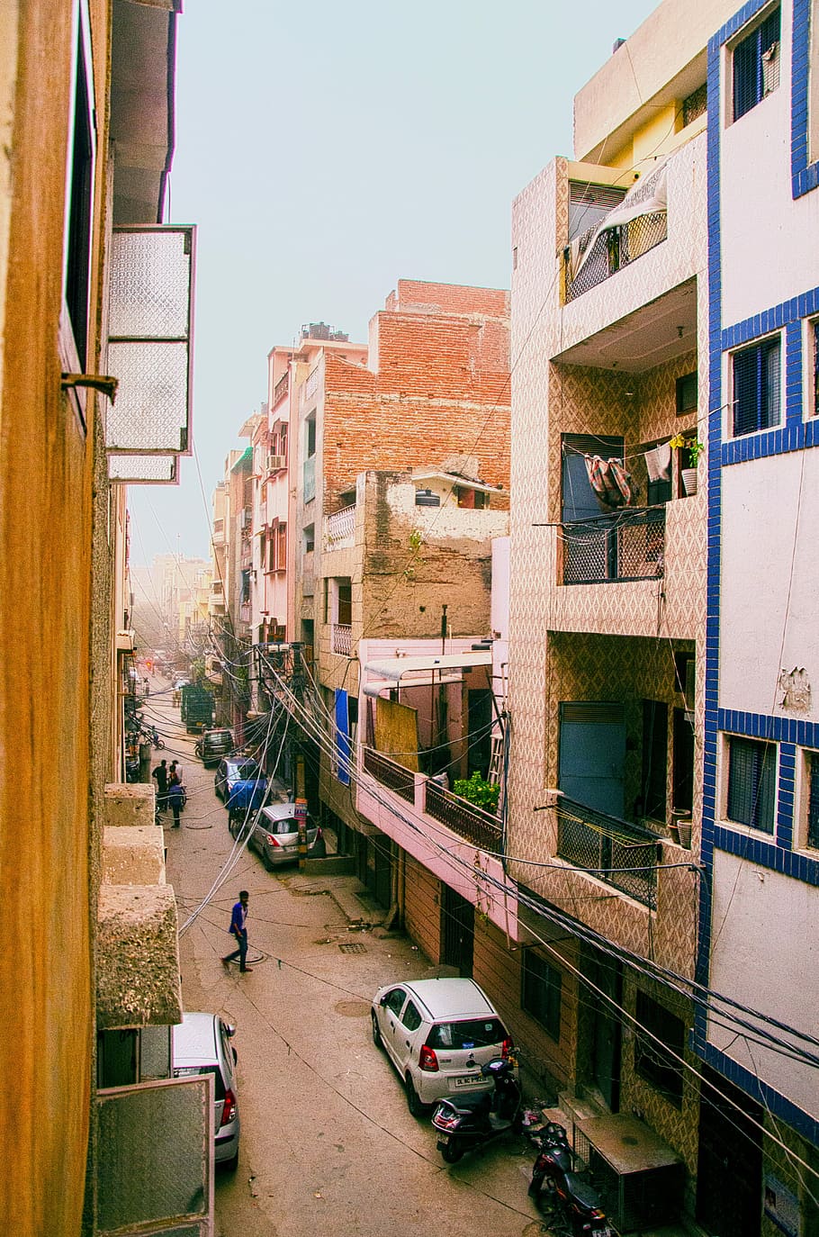 vehicles and people on road between buildings, white hatchback parked near building HD wallpaper