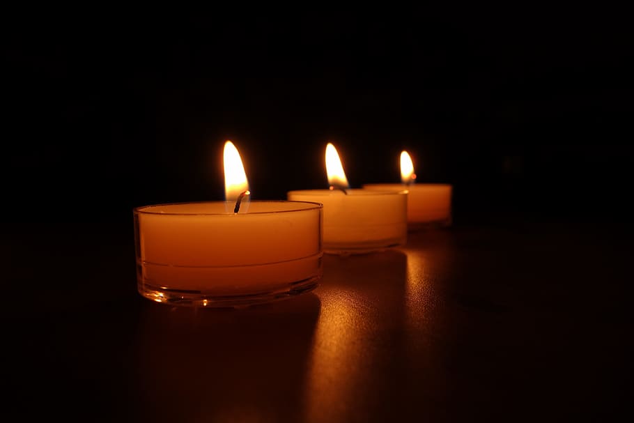 three lighted tealight candles in black room, candlelight, wax