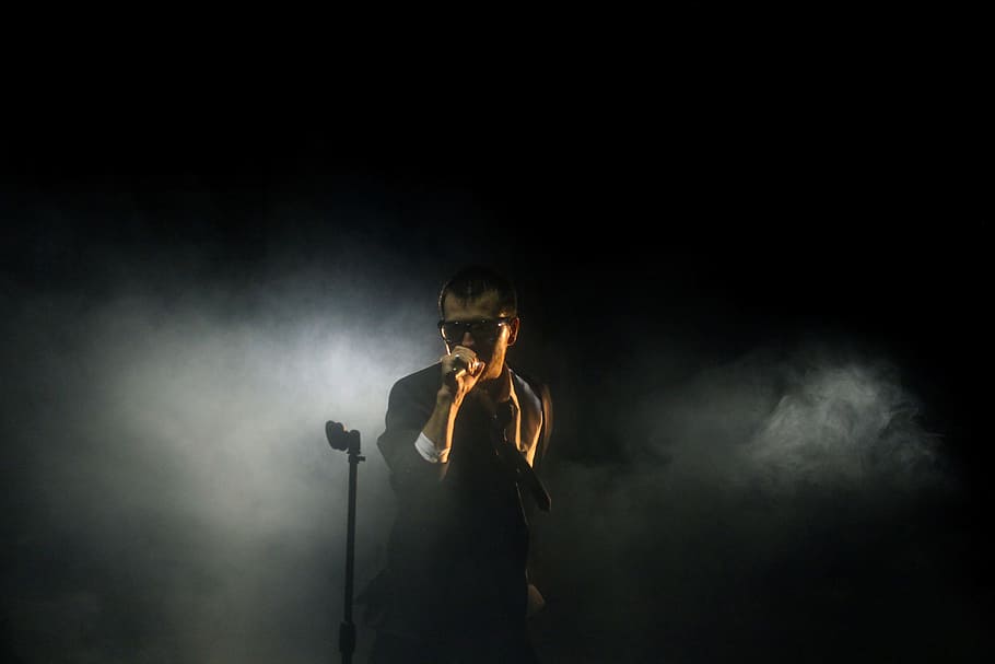 man standing beside microphone stand holding microphone, man wearing black sunglasses using microphone HD wallpaper
