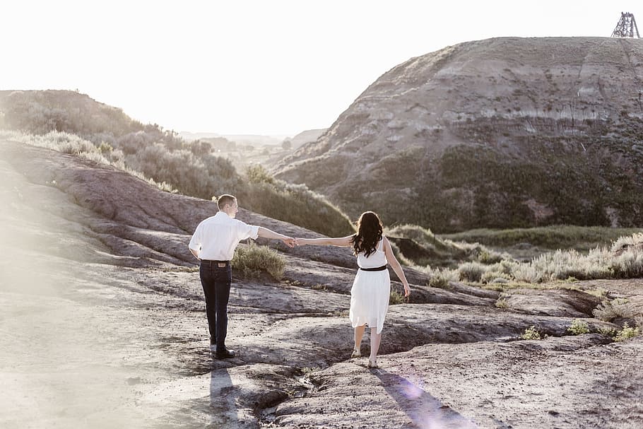 couple holding hands while walking along the rocky coastline, man and woman holding hands while walking on gray mountain during daytime