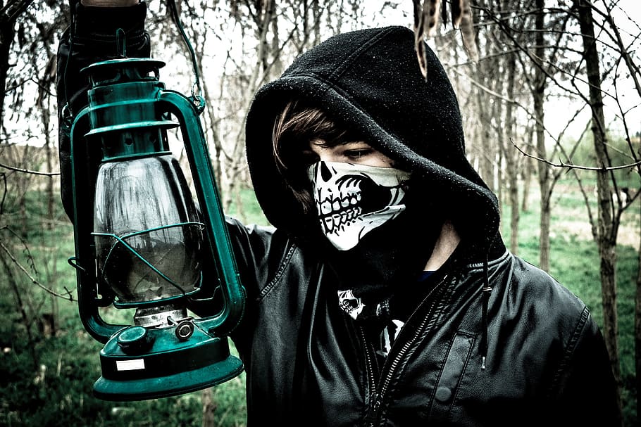 man wearing black hoodie and holding cold-blast lantern near woods outdoors HD wallpaper